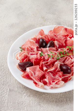 Freshly cut dried meat, served with olives and herbs, on a white plate, light background, no people, Freshly cut dried meat, served with olives and herbs, on a white plate, light background, no people, 126289233