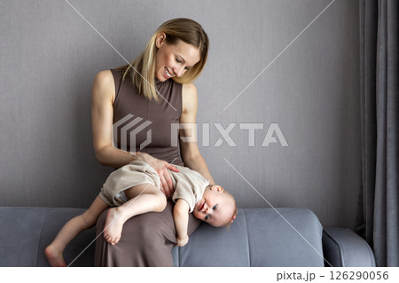 Loving young mother bonding with baby boy at home, sitting on sofa together, enjoying moment in cozy interior. Real family emotions, gentle parenting, trust, authentic motherhood connection indoors Loving young mother bonding with baby boy at home, sitting on sofa together, enjoying moment in cozy interior. Real family emotions, gentle parenting, trust, authentic motherhood connection indoors 126290056