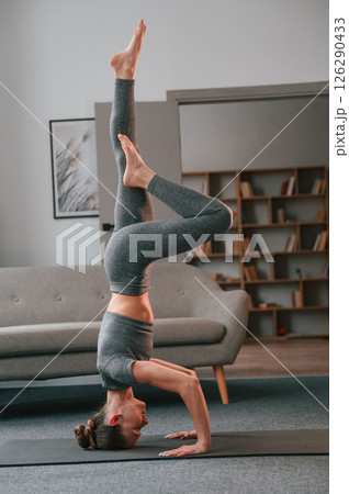 Making headstand. Young woman in yoga clothes doing fitness indoors Making headstand. Young woman in yoga clothes doing fitness indoors 126290433