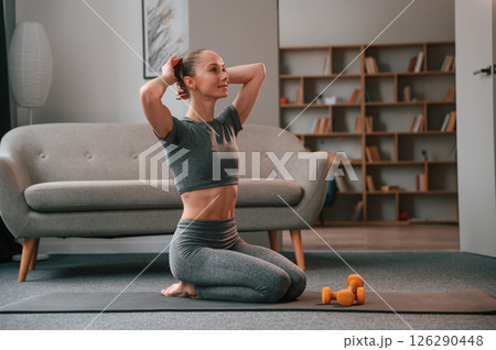 Sitting on the mat. Young woman in yoga clothes doing fitness indoors Sitting on the mat. Young woman in yoga clothes doing fitness indoors 126290448