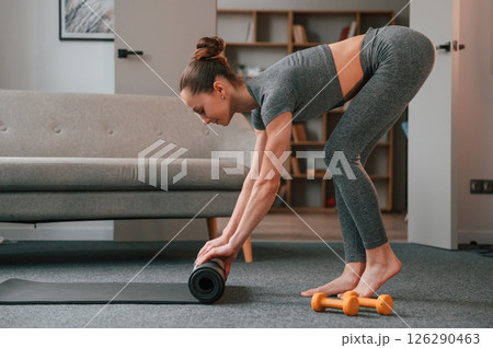 Rolling off the mat. Young woman in yoga clothes doing fitness indoors 126290463