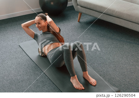 On the mat with foam roller. Young woman in yoga clothes doing fitness indoors On the mat with foam roller. Young woman in yoga clothes doing fitness indoors 126290504