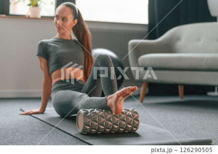 Leg are on the foam roller. Young woman in yoga clothes doing fitness indoors 126290505