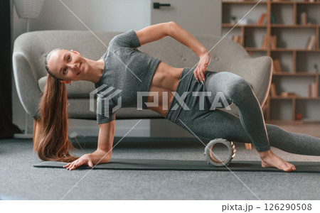 Leg are on the foam roller. Young woman in yoga clothes doing fitness indoors 126290508