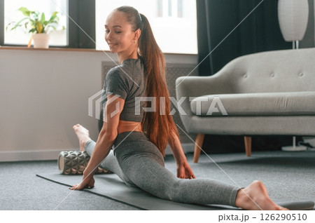 Big stretch for legs. Young woman in yoga clothes doing fitness indoors Big stretch for legs. Young woman in yoga clothes doing fitness indoors 126290510