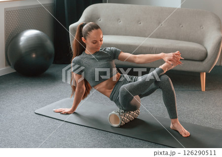 On the mat with foam roller. Young woman in yoga clothes doing fitness indoors On the mat with foam roller. Young woman in yoga clothes doing fitness indoors 126290511