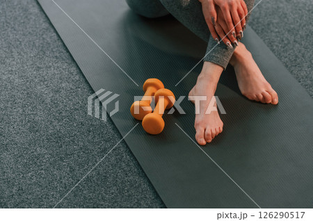 Close up view. Legs and yellow dumbbells. Young woman in yoga clothes doing fitness indoors Close up view. Legs and yellow dumbbells. Young woman in yoga clothes doing fitness indoors 126290517