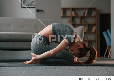 Focused on stretching exercise. Young woman in yoga clothes doing fitness indoors Focused on stretching exercise. Young woman in yoga clothes doing fitness indoors 126290539