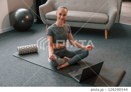 Taking online lessons by using laptop. Young woman in yoga clothes doing fitness indoors 126290544