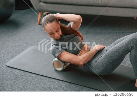 With using the foam roller. Young woman in yoga clothes doing fitness indoors With using the foam roller. Young woman in yoga clothes doing fitness indoors 126290550