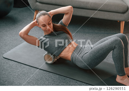 With using the foam roller. Young woman in yoga clothes doing fitness indoors With using the foam roller. Young woman in yoga clothes doing fitness indoors 126290551