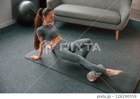 Legs exercises by using foam roller. Young woman in yoga clothes doing fitness indoors 126290559