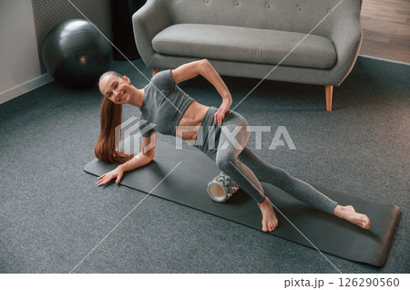 Legs exercises by using foam roller. Young woman in yoga clothes doing fitness indoors 126290560