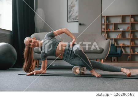 On the right hand and leg on the foam roller. Young woman in yoga clothes doing fitness indoors 126290565