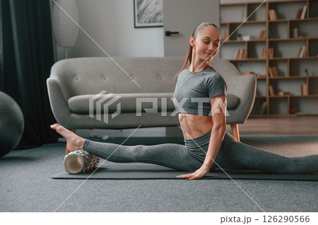 On the mat with foam roller. Young woman in yoga clothes doing fitness indoors On the mat with foam roller. Young woman in yoga clothes doing fitness indoors 126290566