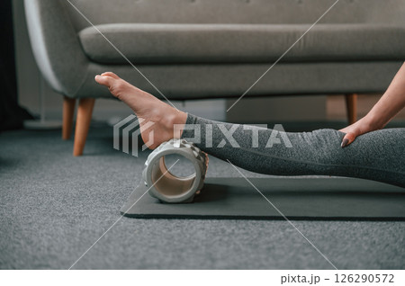 Close up view of leg that is on the foam roller. Young woman in yoga clothes doing fitness indoors Close up view of leg that is on the foam roller. Young woman in yoga clothes doing fitness indoors 126290572