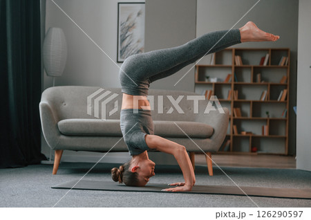 Making headstand. Young woman in yoga clothes doing fitness indoors Making headstand. Young woman in yoga clothes doing fitness indoors 126290597