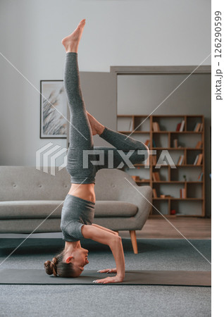 Making headstand. Young woman in yoga clothes doing fitness indoors Making headstand. Young woman in yoga clothes doing fitness indoors 126290599