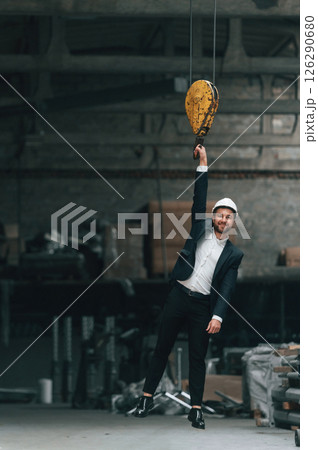 Hanging on the crane hook. Manager in black formal wear at the factory Hanging on the crane hook. Manager in black formal wear at the factory 126290680