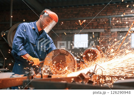 In protective shield on head. Welding the metal. Factory worker in blue uniform is indoors In protective shield on head. Welding the metal. Factory worker in blue uniform is indoors 126290948