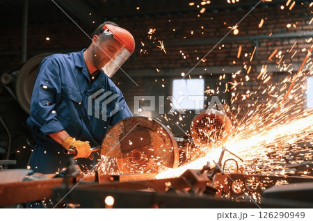 In protective shield on head. Welding the metal. Factory worker in blue uniform is indoors In protective shield on head. Welding the metal. Factory worker in blue uniform is indoors 126290949
