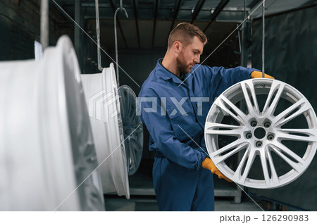 Disk of wheels are hanging. Car service station worker is indoors 126290983