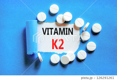 Vitamin K2 phylloquinone symbol. Concept words Vitamin K2 on beautiful white paper. White pills tablets. Beautiful blue background. Medical healthy lifestyle Vitamin K2 phylloquinone concept. 126291261