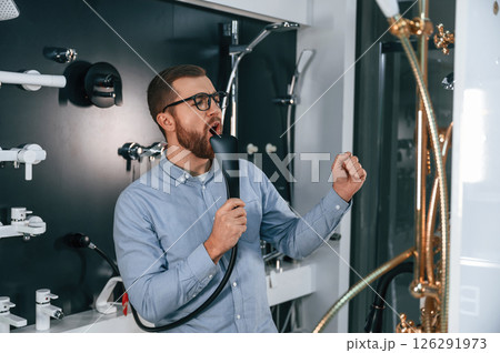 Playing with shower faucet, singing. Man chooses a products in a sanitary ware store 126291973