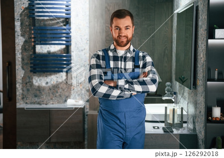 Standing with arms crossed. Plumber in blue uniform is at work in the bathroom Standing with arms crossed. Plumber in blue uniform is at work in the bathroom 126292018