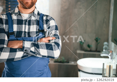 Standing with arms crossed. Plumber in blue uniform is at work in the bathroom 126292019