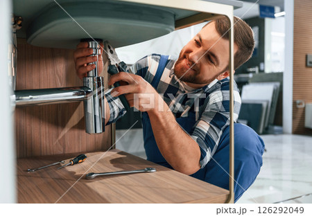 Busy by repairing siphon. Plumber in blue uniform is at work in the bathroom 126292049