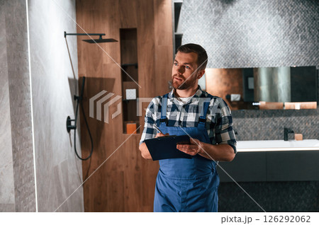 Writes down information in a notebook. Plumber in blue uniform is at work in the bathroom 126292062