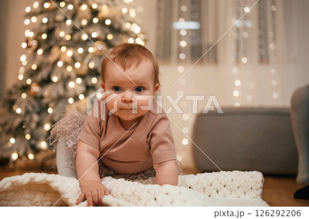 Cute little baby girl is indoors celebrating New Year. Christmas decorations Cute little baby girl is indoors celebrating New Year. Christmas decorations 126292206