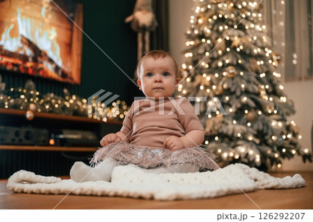 Cute little baby girl is indoors celebrating New Year. Christmas decorations Cute little baby girl is indoors celebrating New Year. Christmas decorations 126292207