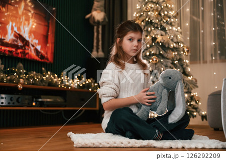 Holding toy in hands. Portrait of little girl that is at home celebrating new year Holding toy in hands. Portrait of little girl that is at home celebrating new year 126292209