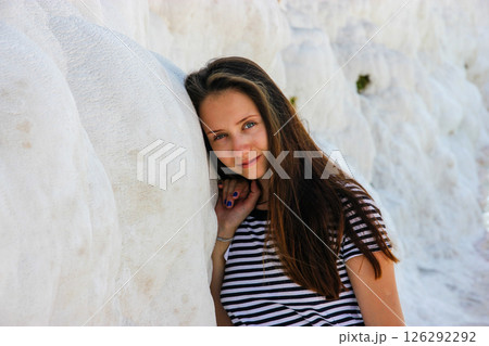 Beautiful young woman with brown hair posing at the white travertine terraces of Pamukkale, looking into the camera with a slight smile. Travel girl. 126292292