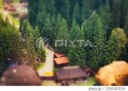 A winding path leads to cabins surrounded by lush green trees in a beautiful mountainous landscape. A high-angle shot showcases picturesque landscape. 126292324