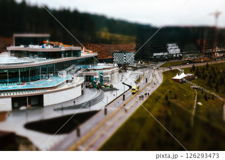 A modern resort and spa complex with swimming pools and a water slide, nestled in a natural setting surrounded by trees. A glass facade exterior. 126293473