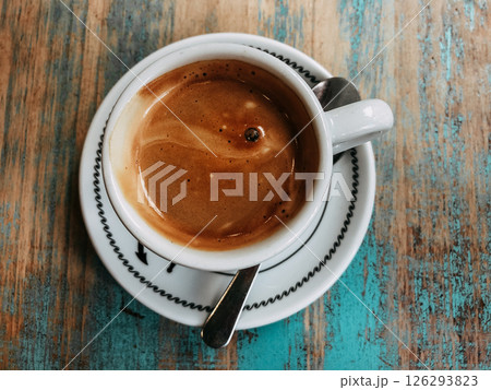 Cup of hot freshly brewed coffee, cappuccino, espresso in white cup on blue textured wooden table top view. Drinking beverage in cafe, coffee shop. Cup of hot freshly brewed coffee, cappuccino, espresso in white cup on blue textured wooden table top view. Drinking beverage in cafe, coffee shop. 126293823
