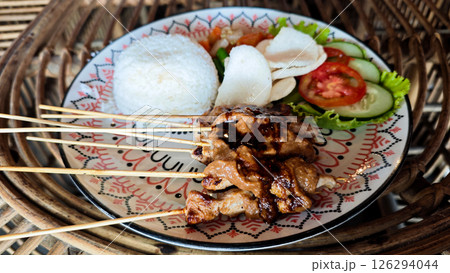 Traditional Indonesian Satay Plate with Rice, Fresh Vegetables, and Peanut Sauce on Decorative Dish on Rattan Table Setting with Vibrant Colors Traditional Indonesian Satay Plate with Rice, Fresh Vegetables, and Peanut Sauce on Decorative Dish on Rattan Table Setting with Vibrant Colors 126294044