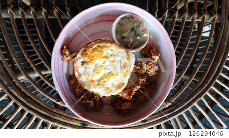 Golden fried egg served with crispy chicken bites and creamy mushroom sauce in a vibrant ceramic bowl, styled on a rustic rattan table, capturing a cozy cafe breakfast ambiance. 126294046