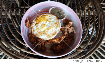 Golden fried egg served with crispy chicken bites and creamy mushroom sauce in a vibrant ceramic bowl, styled on a rustic rattan table, capturing a cozy cafe breakfast ambiance. Golden fried egg served with crispy chicken bites and creamy mushroom sauce in a vibrant ceramic bowl, styled on a rustic rattan table, capturing a cozy cafe breakfast ambiance. 126294047