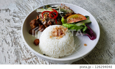 Crispy Fried Pork with Steamed Rice and Fresh Sambal Matah, Served with Salad Garnish on a Rustic Wooden Table Crispy Fried Pork with Steamed Rice and Fresh Sambal Matah, Served with Salad Garnish on a Rustic Wooden Table 126294048