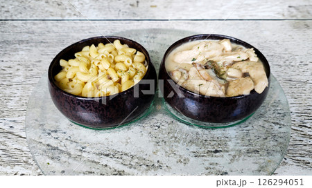 Two Ceramic Bowls with Macaroni Pasta and Creamy Mushroom Chicken on Glass Plate with Rustic Wooden Background Two Ceramic Bowls with Macaroni Pasta and Creamy Mushroom Chicken on Glass Plate with Rustic Wooden Background 126294051