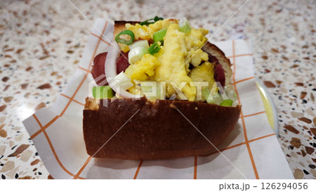 Scrambled egg breakfast sandwich with sausage, green onions, and onions on a soft bun, served on a patterned countertop, perfect for a quick morning bite. Scrambled egg breakfast sandwich with sausage, green onions, and onions on a soft bun, served on a patterned countertop, perfect for a quick morning bite. 126294056