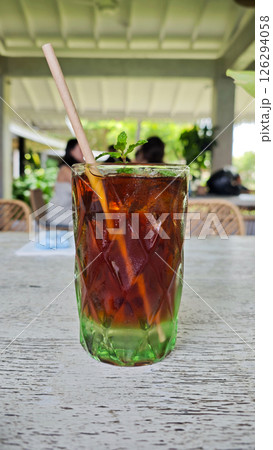 Refreshing Iced Black Tea with Mint Garnish in Textured Glass on Rustic Wooden Table at an Outdoor Cafe Setting Refreshing Iced Black Tea with Mint Garnish in Textured Glass on Rustic Wooden Table at an Outdoor Cafe Setting 126294058