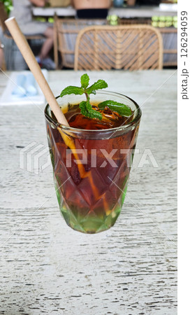 Refreshing Iced Black Tea with Mint Garnish in Textured Glass on Rustic Wooden Table at an Outdoor Cafe Setting Refreshing Iced Black Tea with Mint Garnish in Textured Glass on Rustic Wooden Table at an Outdoor Cafe Setting 126294059