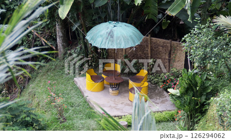 Cozy Outdoor Seating Area with Yellow Drum Chairs and Umbrella in a Tropical Garden Setting Surrounded by Greenery and Bamboo Fence Cozy Outdoor Seating Area with Yellow Drum Chairs and Umbrella in a Tropical Garden Setting Surrounded by Greenery and Bamboo Fence 126294062