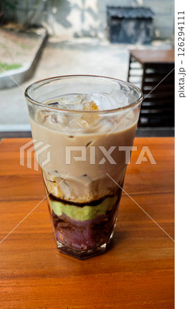 Layered Avocado Mocha Drink with Ube and Sweet Toppings in a Glass on a Wooden Table in an Outdoor Setting 126294111