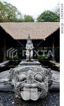 Traditional Balinese Water Fountain Statue with Stone Carvings and Thatch Roof Pavilion Surrounded by Greenery in Tropical Garden Setting Traditional Balinese Water Fountain Statue with Stone Carvings and Thatch Roof Pavilion Surrounded by Greenery in Tropical Garden Setting 126294114